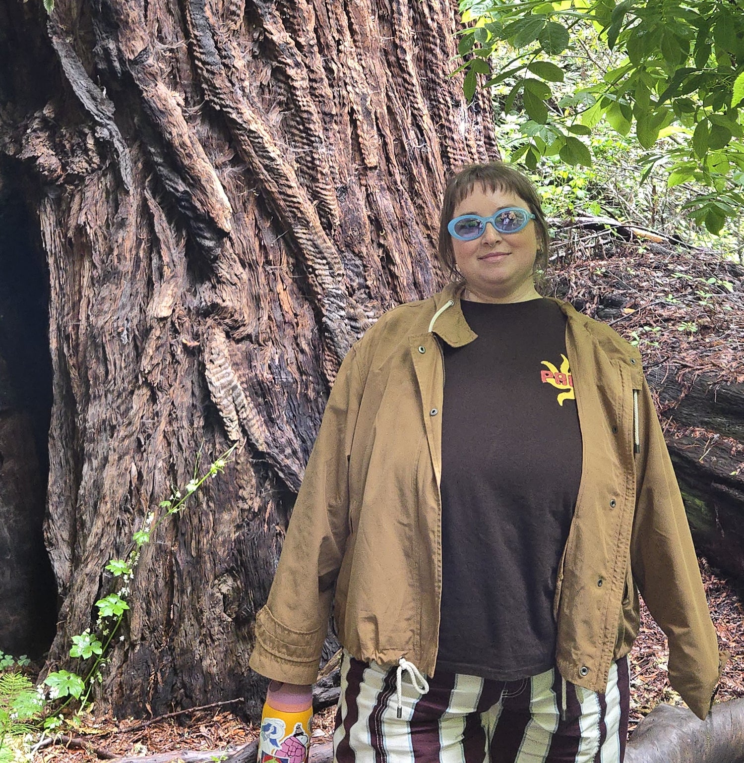 A person (Beck) standing against a large tree smiling (decorative)